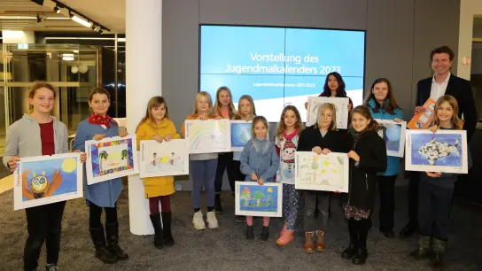 Stolz präsentieren die Kinder und Jugendlichen den Jugendmalkalender 2023 mit Bankvorstand Klaus Berger. (Foto: VR Bank)